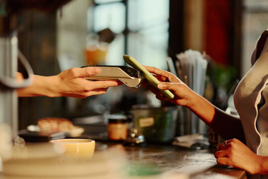 Close up of African American young woman making contactless payment with smartphone at POS terminal. Image suitable for mobile banking and fintech ads