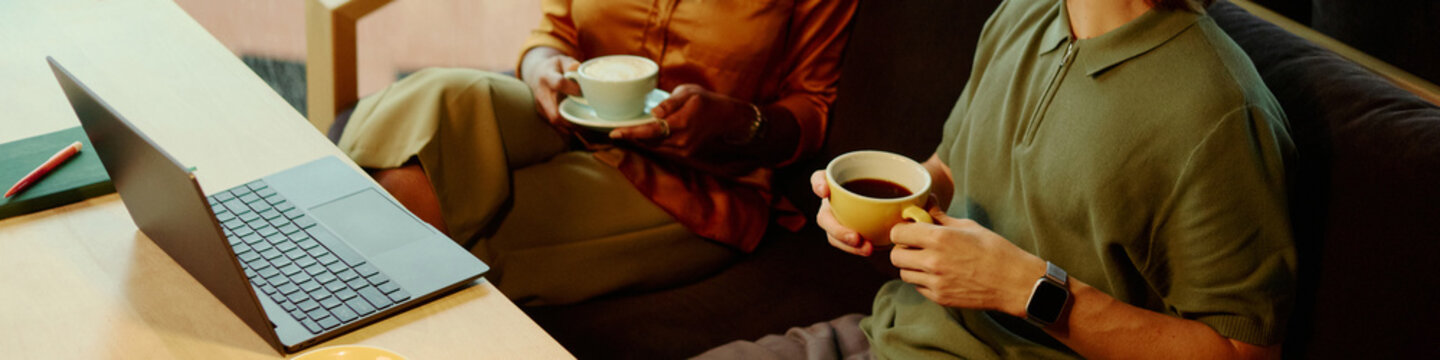 Header of diverse young colleagues drinking coffee while collaborating near laptop during informal meeting. Suitable for remote work, team collaboration and corporate technology campaigns