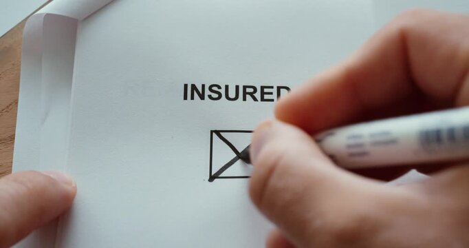 Close-up of a hand marking the insured checkbox on a paper form, representing insurance coverage and policy status.