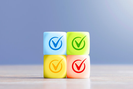 Four colorful blocks with check mark icons on wooden table. Business approval, quality control and task completion concept for success and verification.