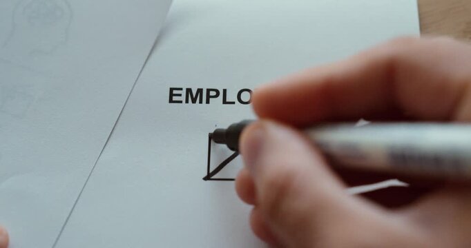 Close-up of a hand marking the employed checkbox on a paper form, representing employment and current job status.