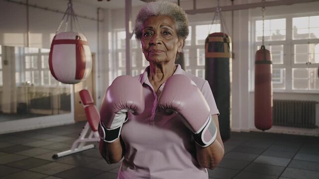 Starting with raised gloves senior woman in pink polo shirt shadowboxing in gym for fitness, gloves