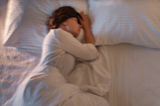 Woman over 40 lying awake in bed at night, symbolizing insomnia, poor sleep quality, exhaustion, anxiety and midlife hormonal changes, blurred image in motion, anxiety