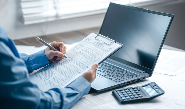 A professional accountant is taking notes on a clipboard regarding tax forms placed next to a laptop and a calculator, covering corporate tax filing, electronic tax filing, financial consulting servic