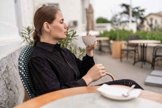 Serene woman holding coffee cup while relaxing at a quiet outdoor cafe garden during the day