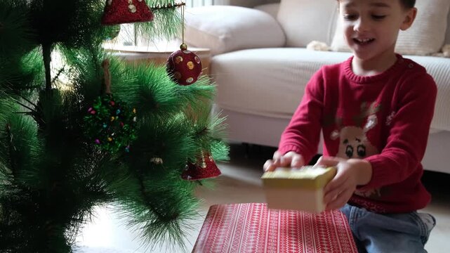 Excited little boy opening christmas present under tree