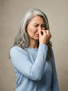 Senior Asian Woman Pinching Her Nose Expressing Disgust or Reacting to a Bad Smell Against Neutral Background