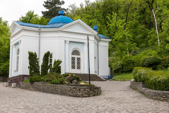 Small white pavillion topped with a blue dome nestled in a green park, featuring classical columns, arched doorway and stone steps of The Cascade Staircase, Zheleznovodsk
