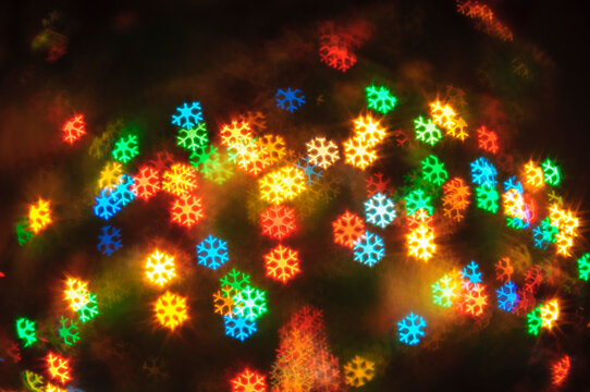 Holiday background. Colorful snowflake shaped bokeh lights on a black background. Blurred red, blue, green and yellow glowing shapes in a festive night pattern