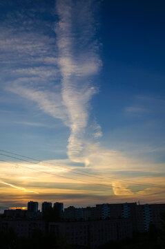 City sunset urban background. A golden and blue sky with wispy clouds and aircraft contrails above residential buildings. Diagonal power lines across the frame