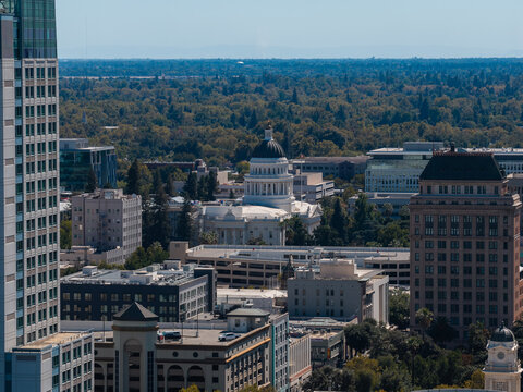 Aerial shot of downtown Sacramento displaying the historic California State Capitol building encircled by urban offices and forest canopy reaching toward the horizon on a clear day.