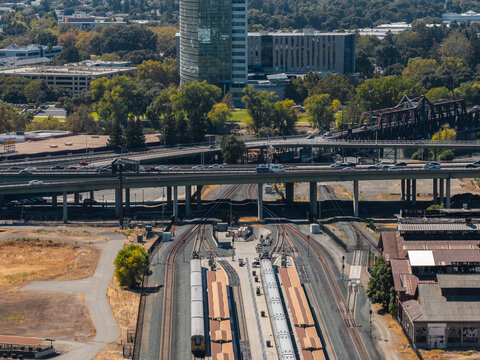 Aerial view shows passenger trains at Sacramento Valley Station platforms beneath an interstate freeway overpass with city architecture and rail infrastructure in California.