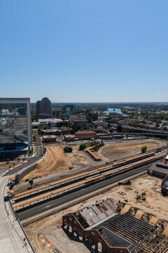 Aerial perspective looking across the Sacramento Valley Station railroad tracks, historic railyard structures under renovation, and downtown Sacramento cityscape along the Sacramento River.