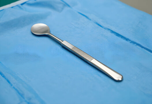 Medical examination and surgical procedure, stainless steel curette tool on blue sterile drape for clinical healthcare and hospital surgery preparation