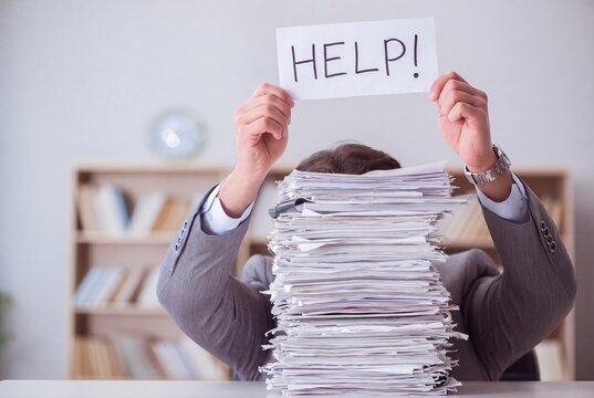 Stressed businessman holding help sign behind a massive stack of paperwork, corporate burnout and workload pressure in office