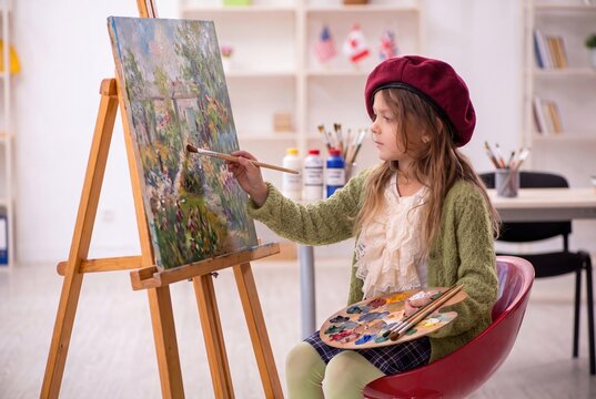 Creative little girl painting on canvas with an easel, holding a colorful palette in an art class for kids and creative hobbies