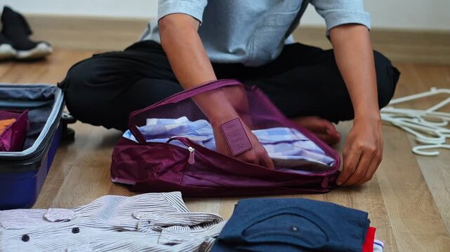 Close-up of hands placing blue plaid shirts into fabric packing pouch and zipping it shut