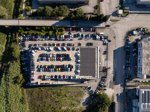 Aerial view of a busy parking lot filled with numerous cars parked in orderly rows, featuring a large solar panel array covering a section of the lot, situated in Ancona, Marche, Italy.