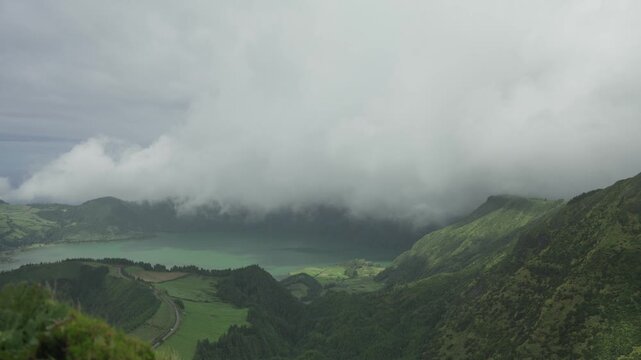 Low clouds roll over the Sete Cidades caldera seen from the Grota do Inferno viewpoint on Sao Miguel, with Lagoa Azul and green pasture below.