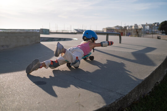 Playful Little Girl Lying on Skateboard Pretending to Fly at Skatepark Outdoors