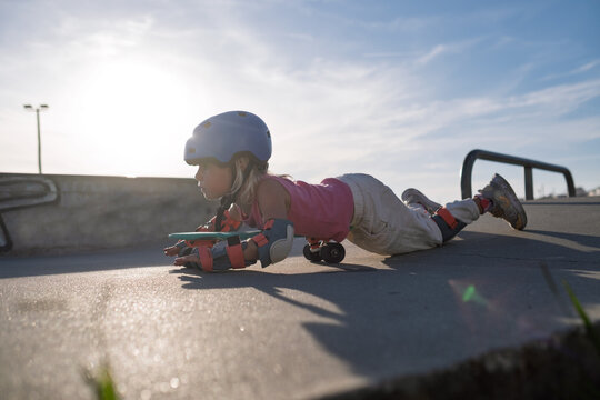 Playful Little Girl Lying on Skateboard Pretending to Fly at Skatepark Outdoors