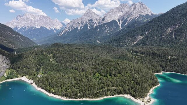 Aerial view frames a broad wooded peninsula bordered by turquoise Blindsee with rugged mountains beyond in the Austrian Tyrol for serene travel films and outdoor backgrounds