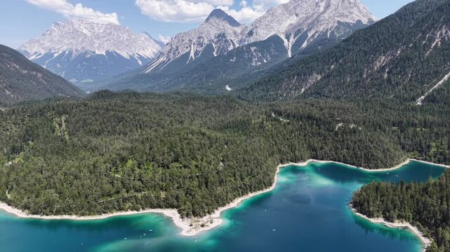 Aerial view reveals the indented shoreline of Blindsee around a wooded headland in the Austrian Tyrol with layered peaks beyond for tranquil tourism videos and scenic backgrounds