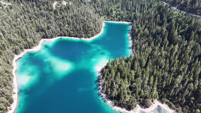 High angle aerial view reveals the irregular outline of turquoise Blindsee enclosed by dense woodland in the Austrian Tyrol for calming nature backgrounds and scenic travel videos