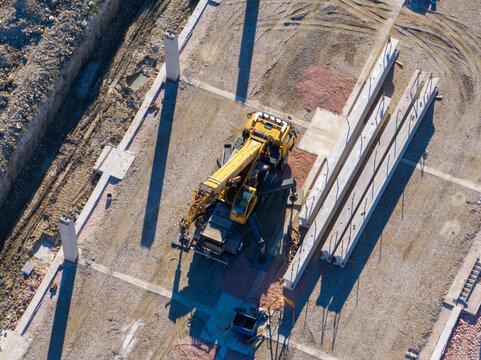 Aerial view of a yellow mobile crane operating at a construction site with concrete beams and gravel ground in Ancona, Marche, Italy.