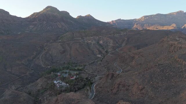 A stunning aerial push in shot of the rugged volcanic landscape on Gran Canaria, featuring the La Solana hamlet and a winding road.