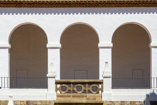 White facade building featuring an arcade with three symmetrical arches and columns, casting strong shadows on a sunny day, showcasing Spanish architectural style