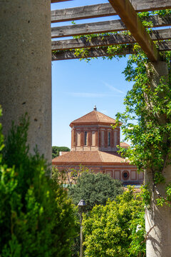  Archaeology Museum of Catalonia and lush green foliage climbing a concrete pillar and wooden pergola providing a natural frame for a distinctive orange-tiled domed building in Barcelona