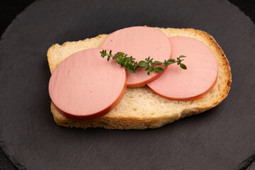 Boiled sausage sandwich on white bread with fresh thyme branch. Bologna sausage slices on bread over black slate plate. Horizontal food e-commerce copy space.  © Inna Nikitina