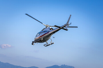 Fototapeta premium A TV broadcast helicopter equipped with camera gear hovering in the blue sky to record live aerial footage.