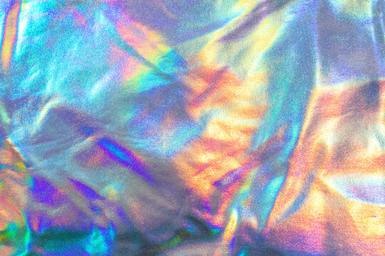 Holographic iridescent metallic fabric texture with colorful shimmering wrinkles and abstract background