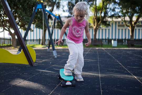 Little Girl in Blue Helmet Learning to Step on Penny Board at Outdoor Playground