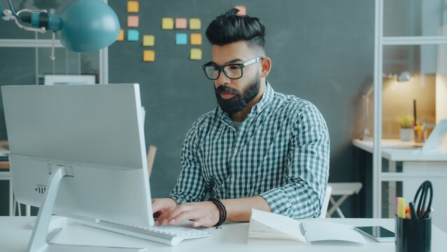 Mixed race guy is suffering from headache touching head working with computer in office at desk. Modern technology and human health concept.