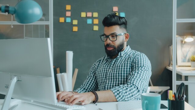 Arab man is working with computer then writing i notebook in office concentrated on job. Coworkintyping, young people and modern technology concept.
