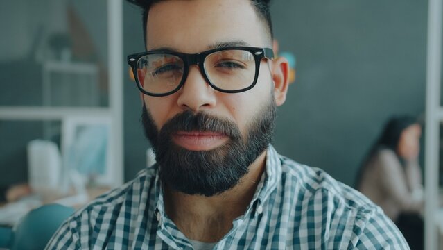 Close-up portrait of handsome Arab man wearing glasses looking at camera with serious face in office. Businesspeople, workspace and coworking concept.