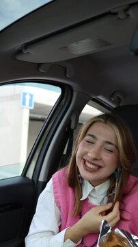 Vertical screen playful young woman tosses a crispy snack toward her mouth but misses and laughs at the funny moment while relaxing as a passenger during a casual car ride