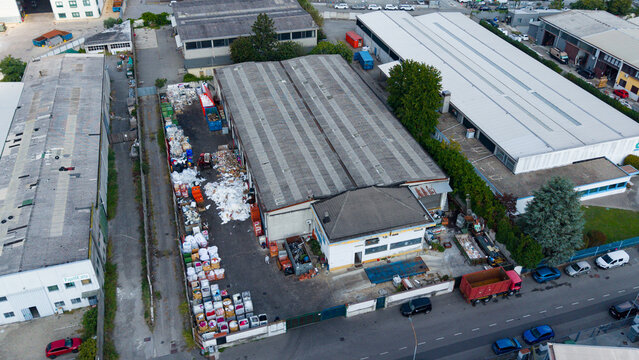 Aerial view of a waste collection and sorting facility with large piles of recyclable materials, industrial buildings, and trucks in Milan, Lombardy, Italy.