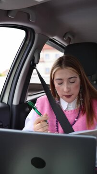 Vertical screen overwhelmed woman works nonstop in a car rushing through notes and laptop tasks as deadlines pile up showing hyperproductivity and constant work pressure