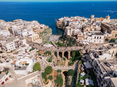 Aerial view of Polignano a Mare featuring the iconic Lama Monachile beach nestled between limestone cliffs, historic white buildings, and a stone bridge in Polignano a Mare, Apulia, Italy.