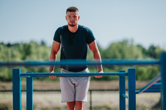 A young man performs dips on outdoor parallel bars as part of a fitness workout. The athletic man trains strength and bodyweight skills at an outdoor exercise area.
