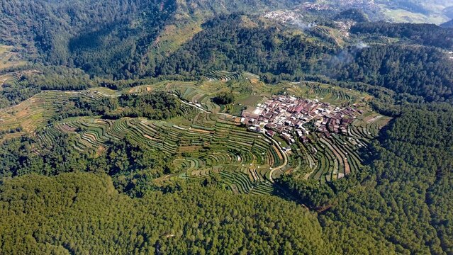 Aerial view of Pagergunung village surrounded by lush terraced farmland and dense forest in the mountains of Ngablak, Central Java, Indonesia.