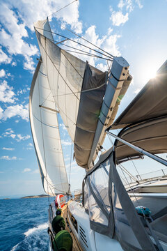 View from deck of sailing yacht with fully deployed sails cruising across Adriatic Sea under bright blue sky. Dynamic maritime travel scene representing freedom, adventure and nautical lifestyle