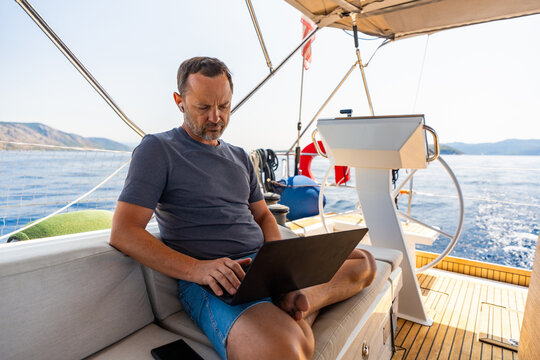 Focused man working on laptop aboard a sailing yacht. Productive remote office in a unique travel environment.
