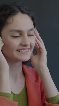 Joyful lady putting on headphones listening to music dancing on black background. Modern technology and entertainment concept.