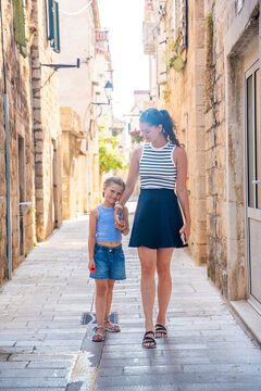 Mother and daughter walking hand in hand through narrow street in Trogir, Croatia. Family travel creates shared experiences and strengthens parent child bond