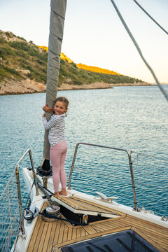 Young girl balancing on bow of sailing yacht near Croatian coast. Childhood adventure at sea represents freedom, confidence, exploration and connection with nature